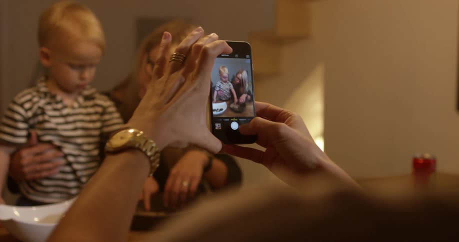 Many people in a kitchen and a woman takes pictures of a baby