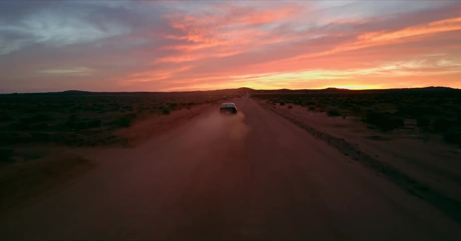 A car travels on a rural dirt road at sunset