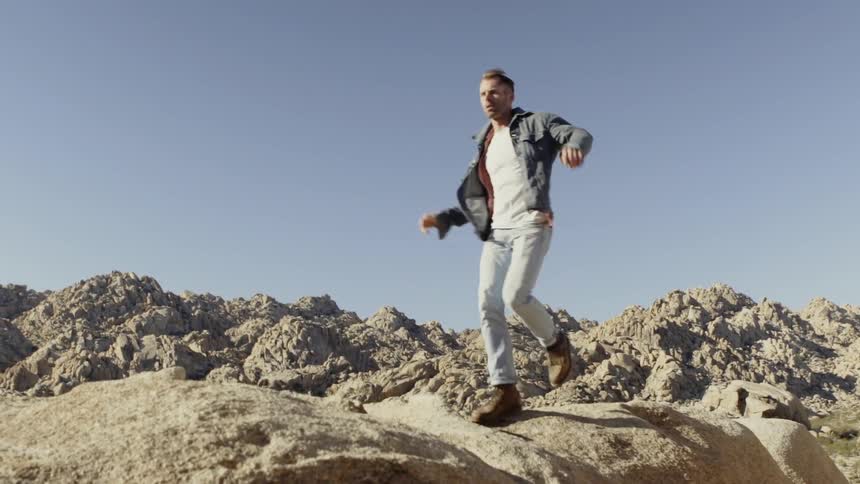 A man jumps downhill over the rocks