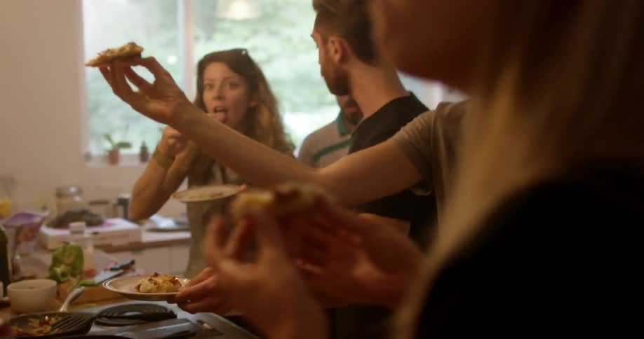 A group of people eating pizza in a kitchen