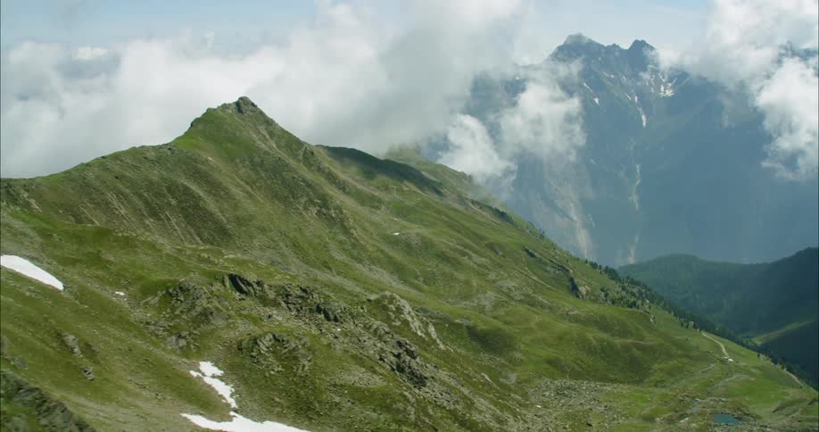 Grass covered mountains have puffy clouds flow over them
