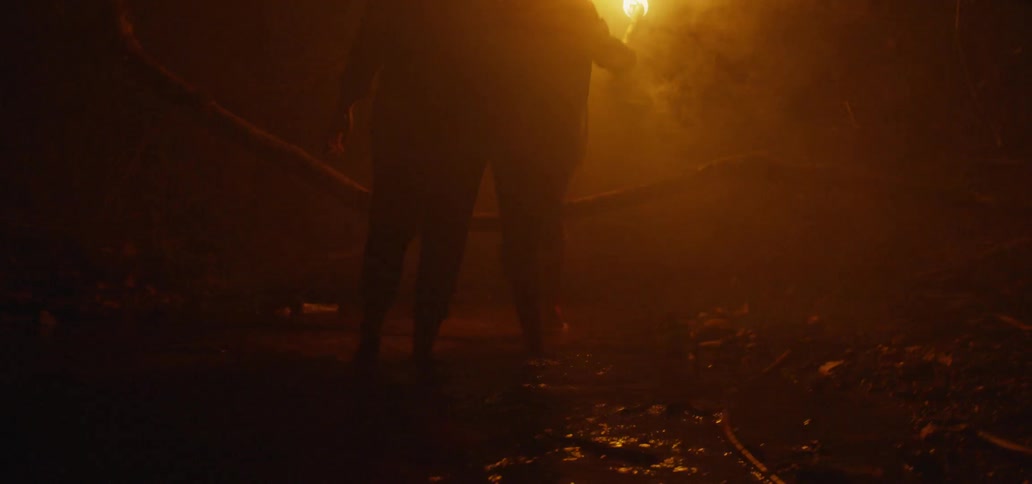 Man and woman walk through the water as the woman carries a torch