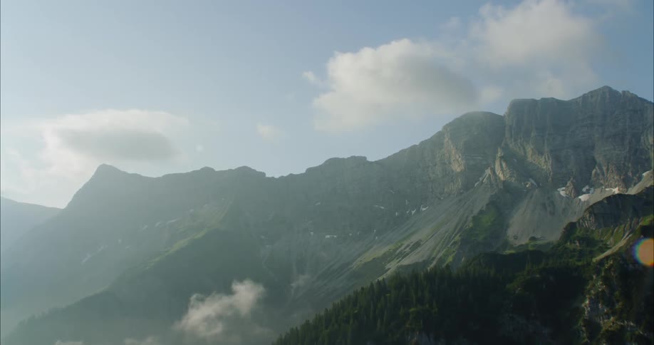 A mountain range with trees sits beneath fluffy clouds