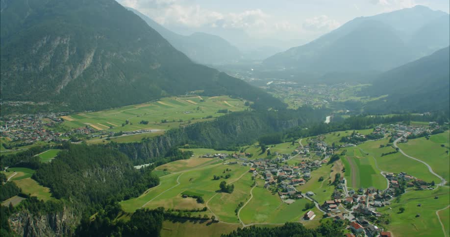 Steep green mountains with small towns in the tree and grass lined valley
