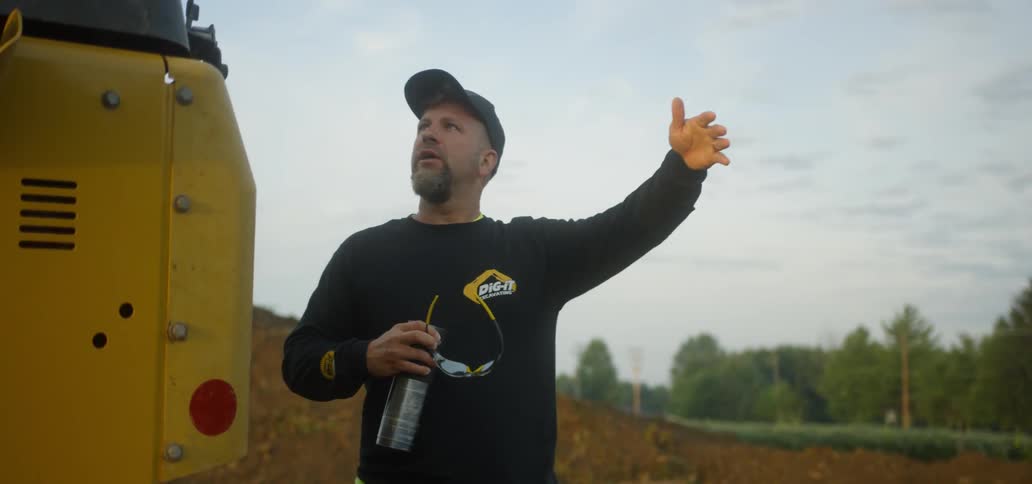 A man is outside wearing a hat talking to someone