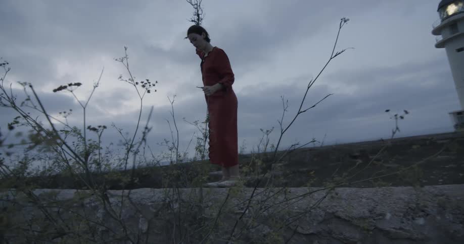 A woman waves a large branch near a lighthouse