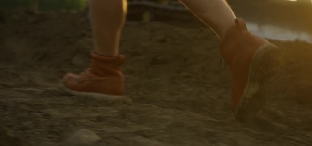 Someone wearing work boots walks in freshly dug earth as a caterpillar pushes more earth in the background