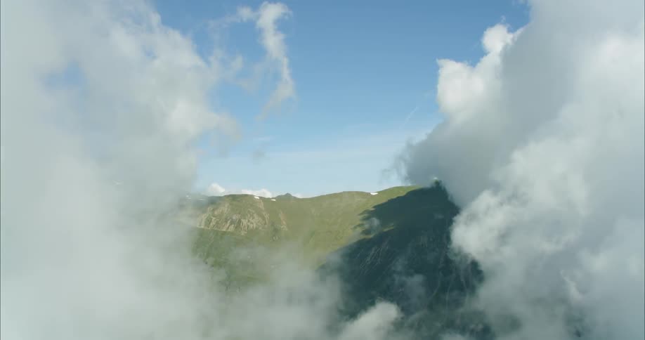 The large white clouds are rolling over the green mountain