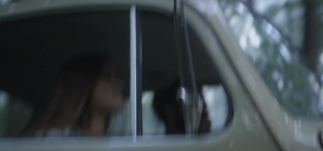 A man and woman ride through the woods in a volkswagen beetle