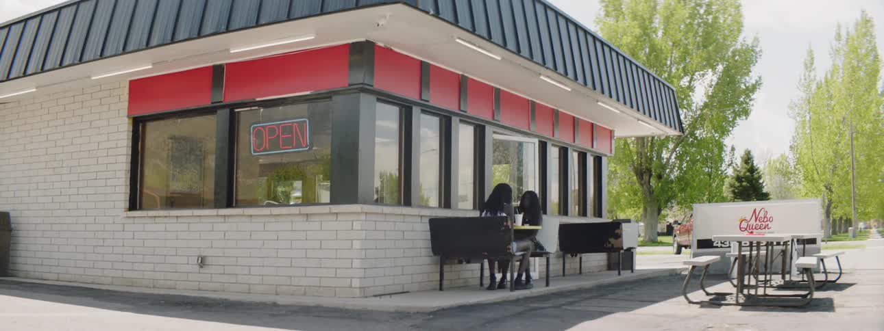 Two women sit beside a restaurant eating at a table