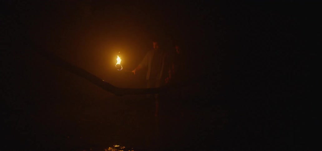 A couple walking together in the darkness as the man carries a torch