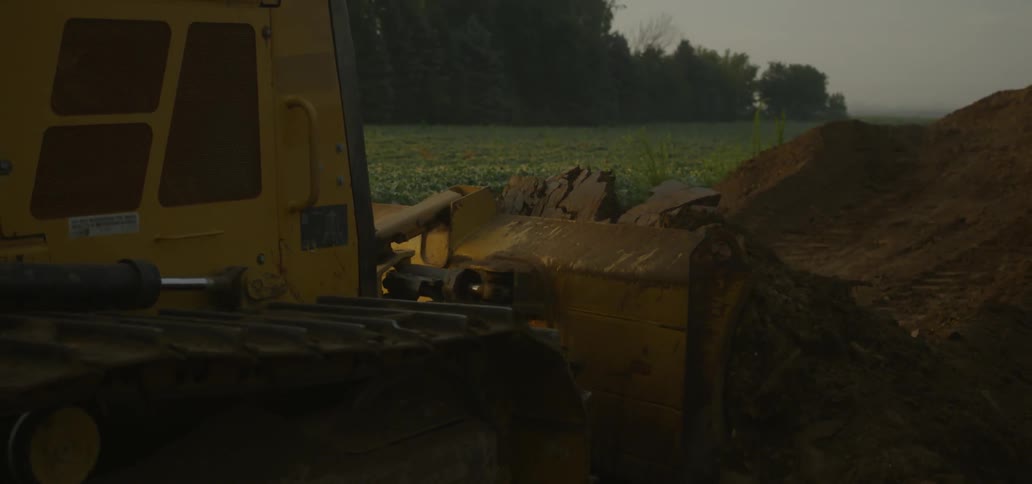 A bulldozer plows through dirt at sunset