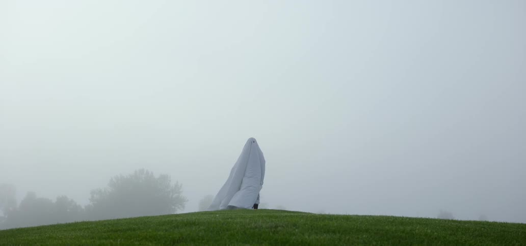 Person wearing white sheet walks away from camera into fog