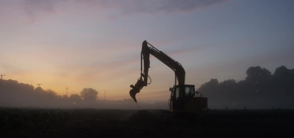Excavator digging in a field during sunset