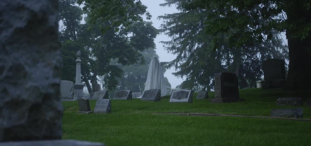 A white sheet-clad figure steps through some gravestones