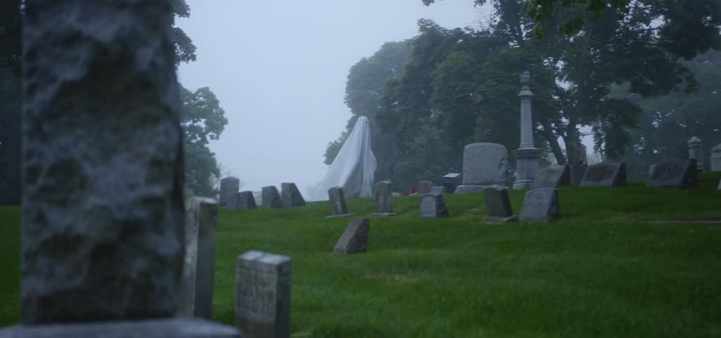 Sheet ghost is walking among graves in the grave yard on a slightly foggy day