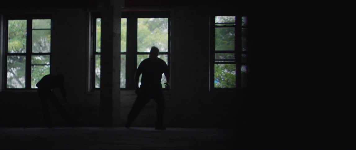 A man kicks another man in a dark room