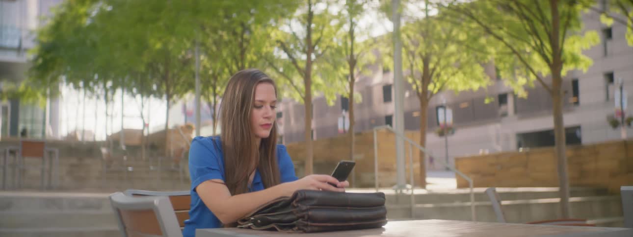 Girl sits outside at a table while on cell phone