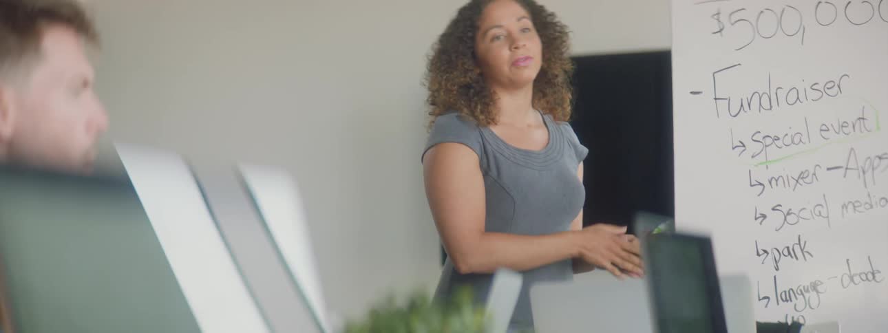 A female stands next to a whiteboard delivering a presentation