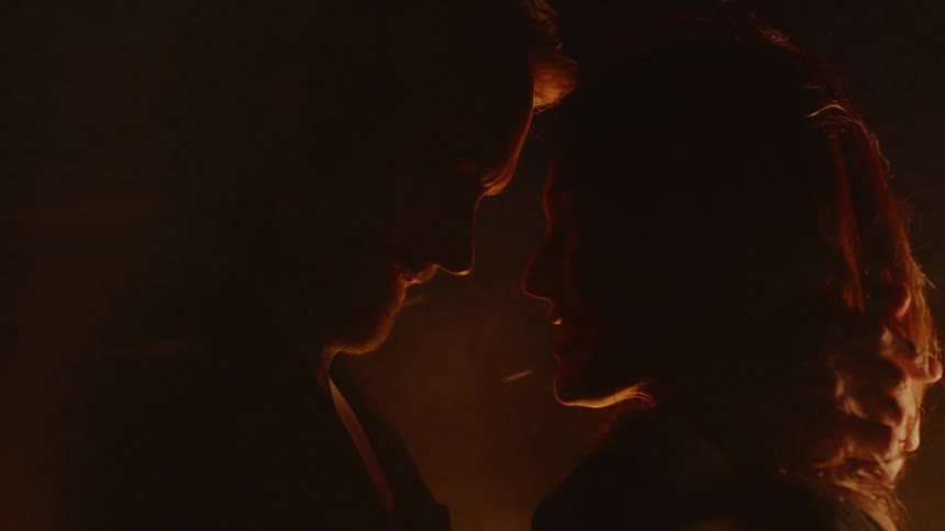 A man and a woman holding each other in the dark while a fire burns