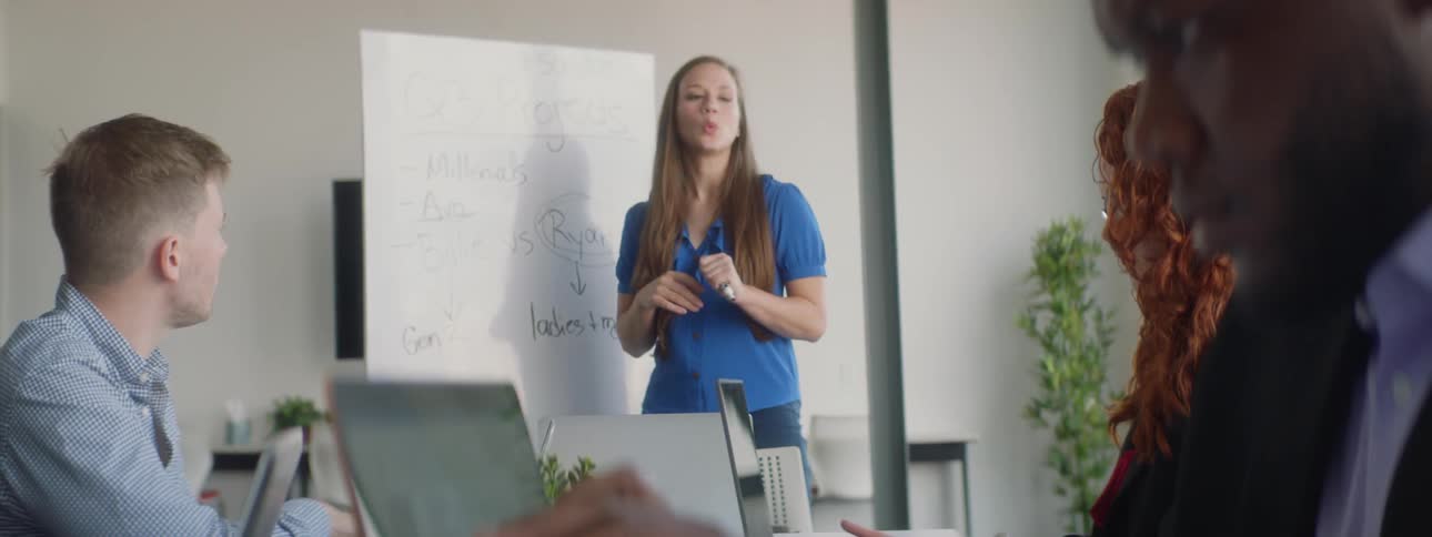 A woman speaks in front of a white board during a work meeting