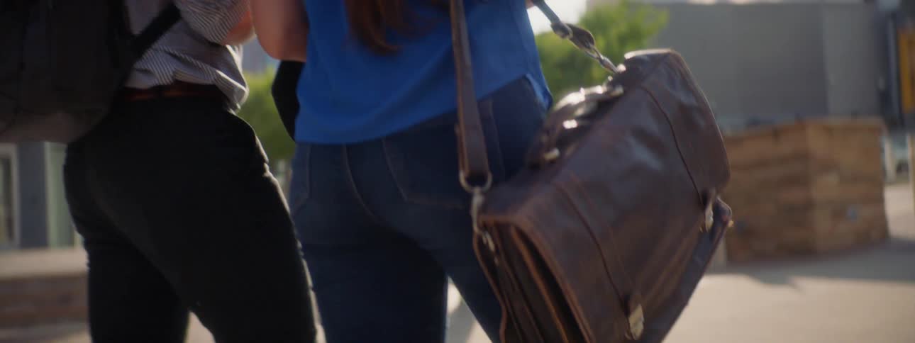 Man wearing a backpack and a woman carrying a briefcase walk under the bright sun