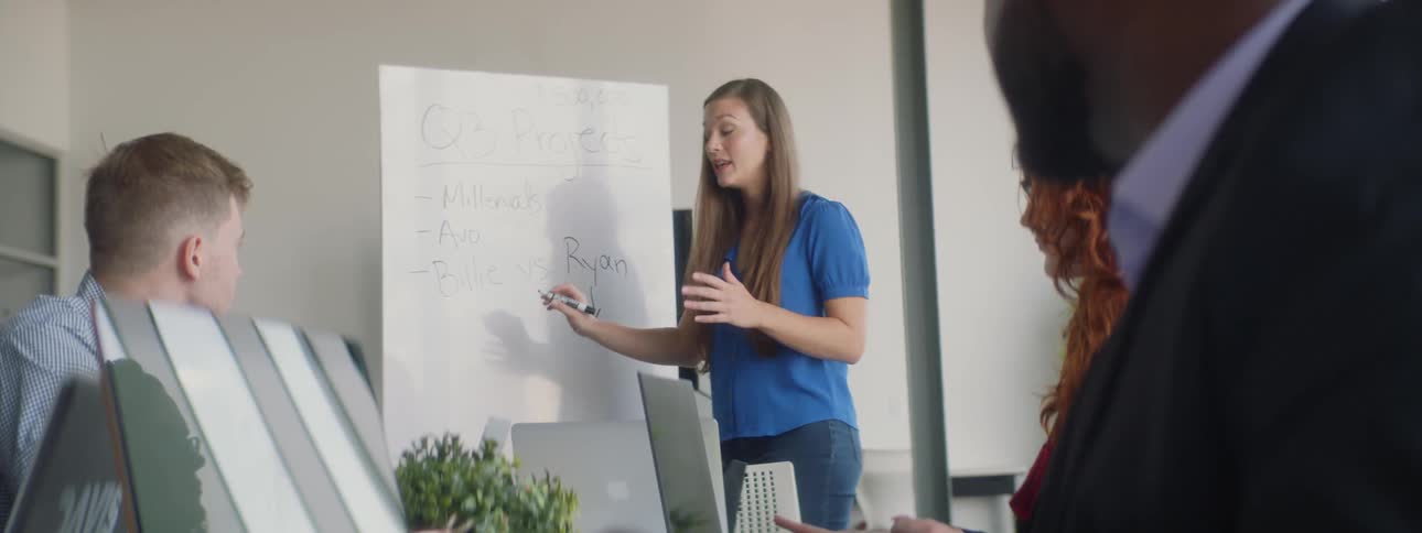 A woman talks with people while writing on a whiteboard