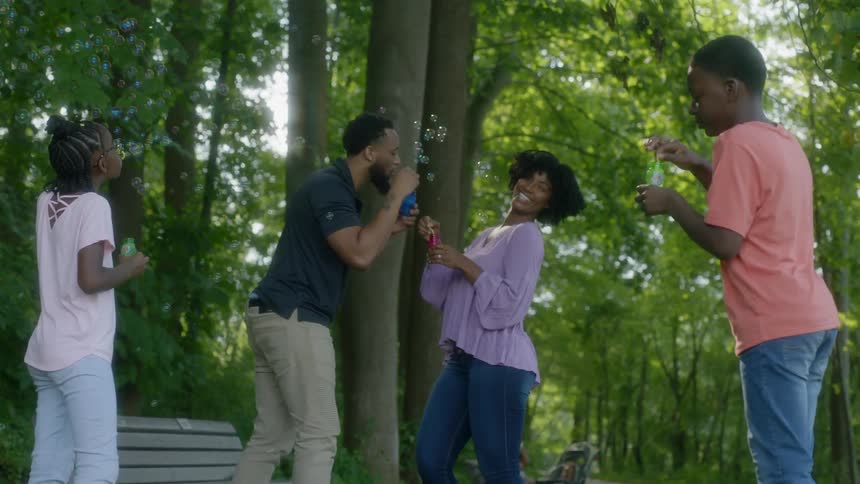 A family of four blowing bubbles while standing on a park pathway
