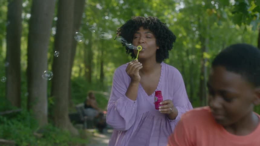 A mom and son blow bubbles in the park