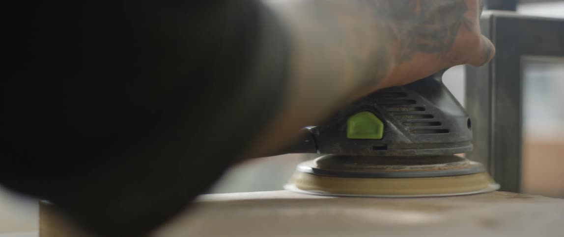 A man smooths wood with a power sander