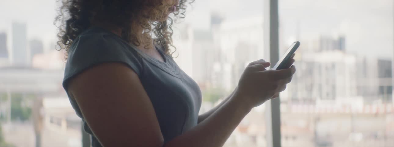 Woman standing near window handles cell phone