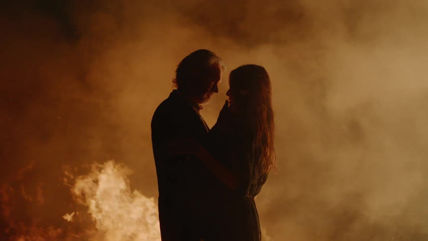 A woman and man are standing close by each other surrounded by fire
