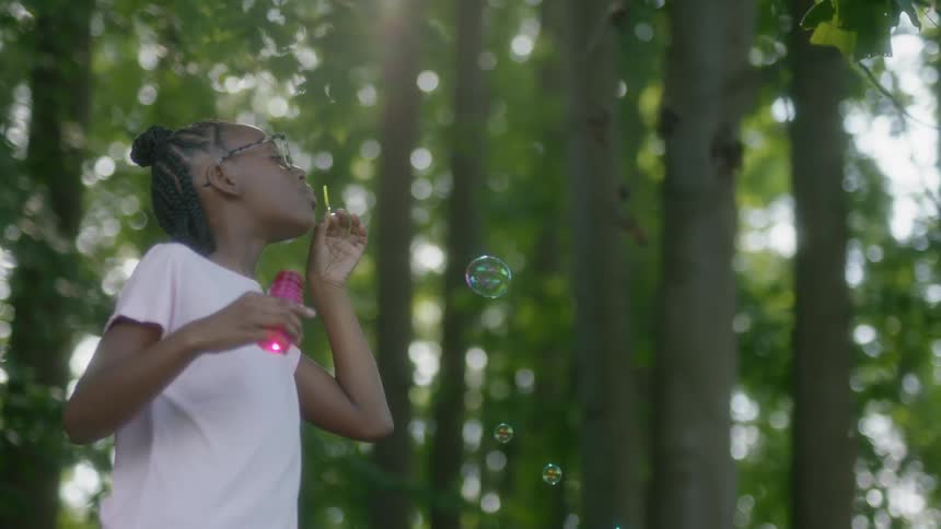 Girl blowing bubbles surrounded by trees