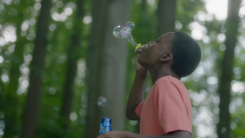 A pre teen male blowing bubbles in a wooded area