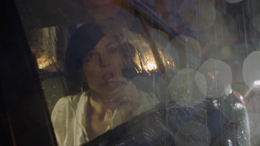 A woman sits in a car during a rainstorm