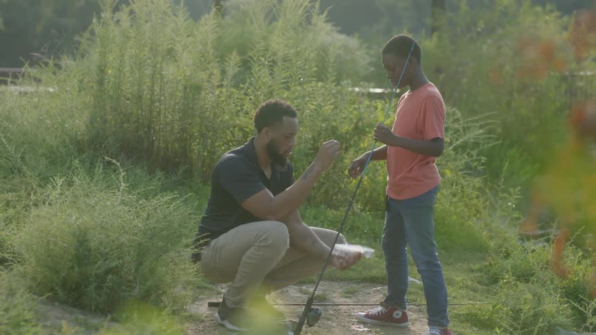 A father showing his son how to put bait on a fishing pole
