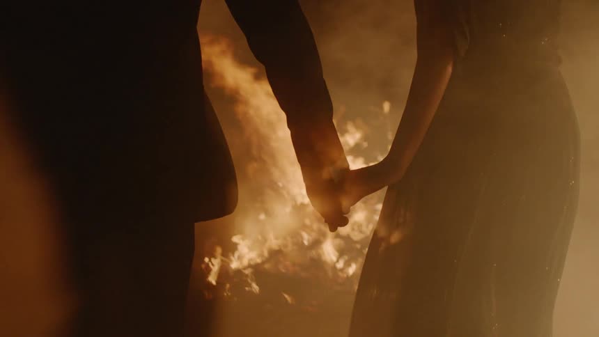 Man and woman are holding hands in front of bonfire at night