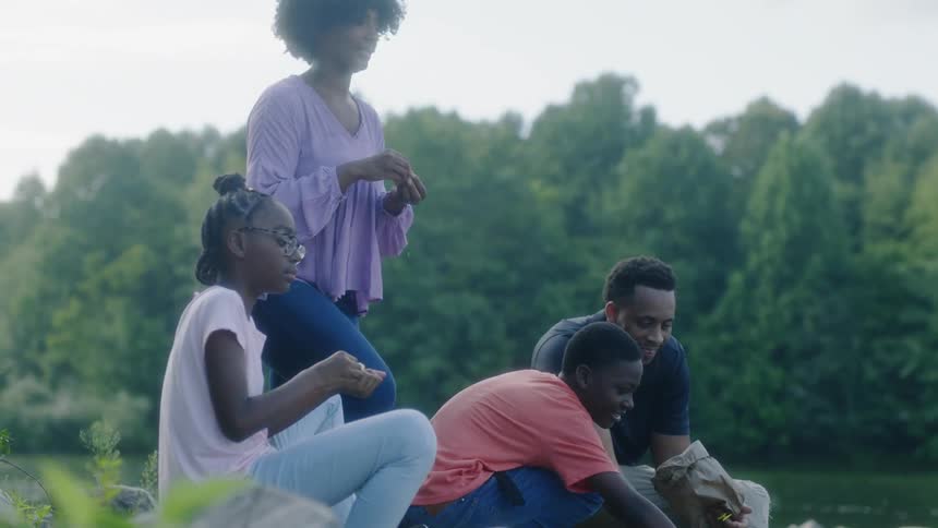 A family of four tossing food from a bag into a river