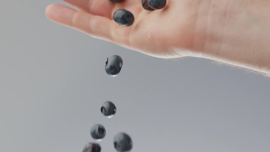 A person is holding blueberries and dropping them