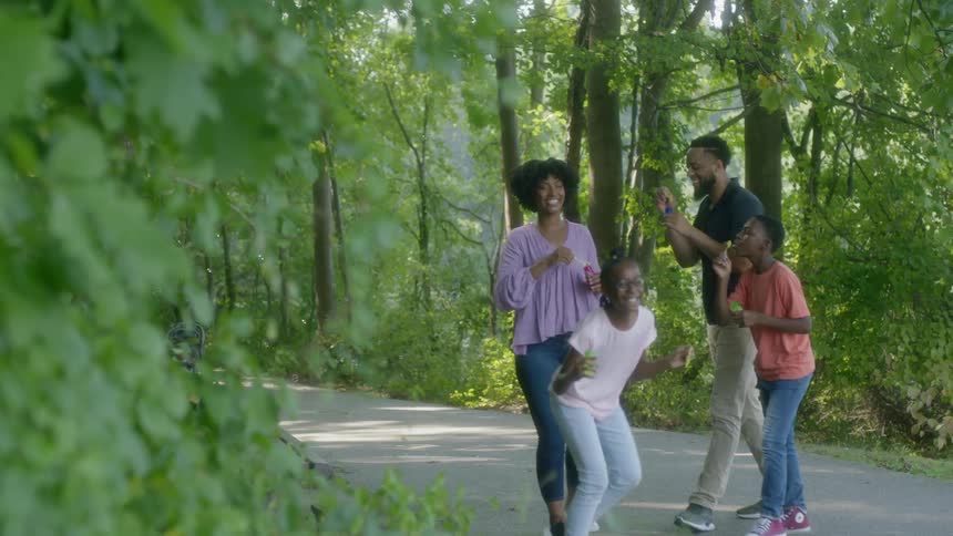 A family of four blowing bubbles while standing on a park pathway