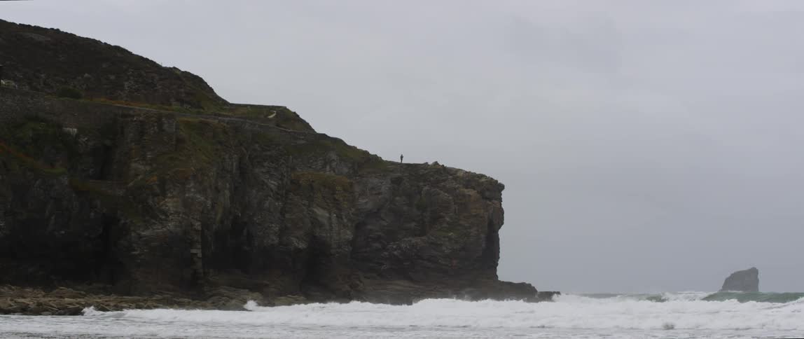 A person stands at the edge of the rocky beach cliff