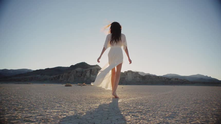 A woman in a white dress walking through a dry desert