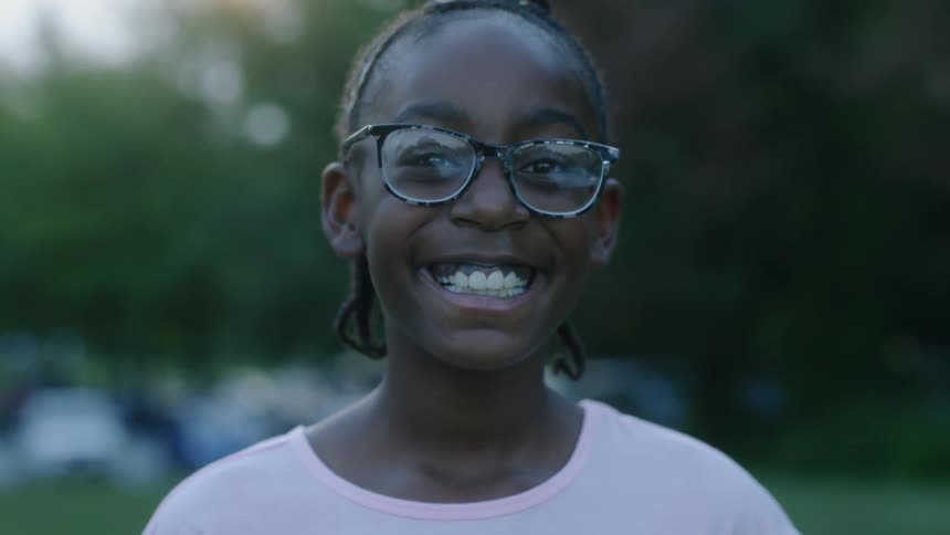 Child smiles standing outside near trees