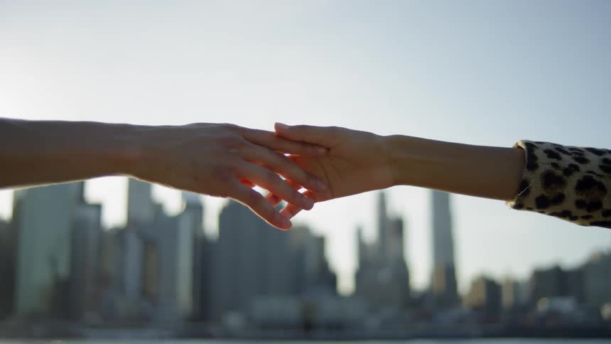 Two hands holding each other in front of New York City