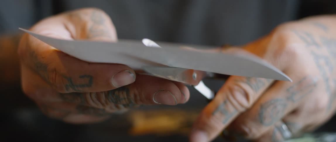 Tattooed hands cut a piece of paper with scissors