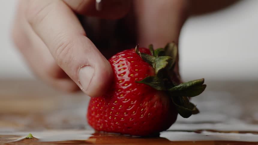 A strawberry being turned by a hand