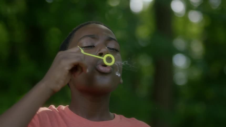A boy blows bubbles outside near trees