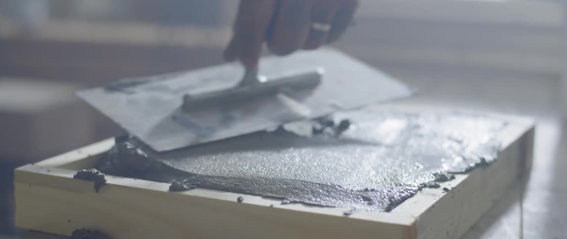 A person smooths cement in a wooden frame with a trowel