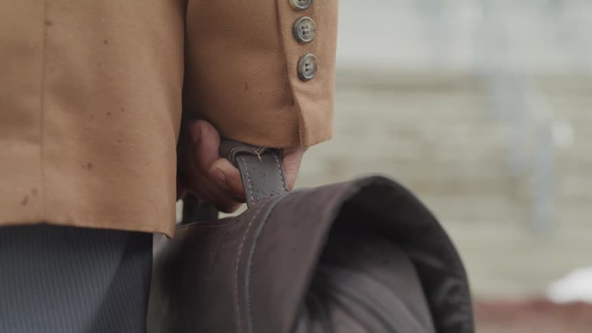 Man standing still and holding leather briefcase at his waist