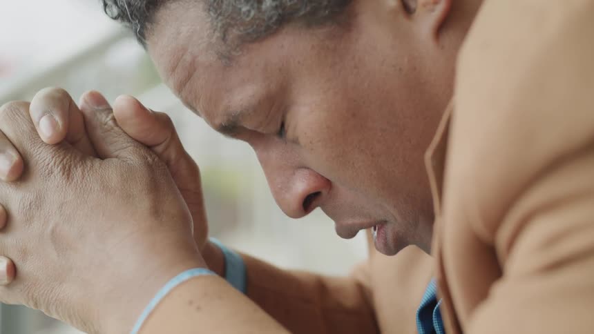 Man with hands cupped and head bowed with an upset expression
